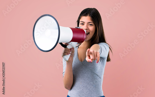 Teenager girl holding a megaphone on pink background