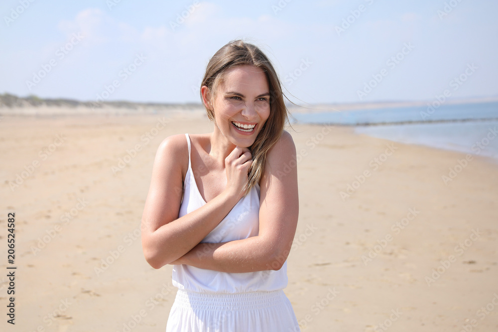 Hübsche blonde Frau steht lachend an einem Strand Wasser im Hintergrund Hübsche blonde Frau steht lachend an einem Strand Wasser im Hintergrund
