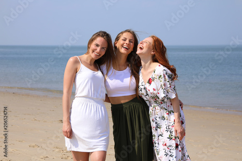 Drei hübsche junge Frauen stehen lachend am Meer