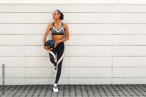 Woman in sportswear relaxing during workout, standing at wall with medicine ball