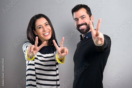 Couple making victory gesture on grey background