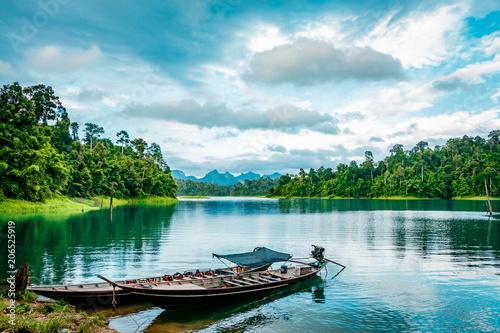 Fototapeta Naklejka Na Ścianę i Meble -  Wooden Thai traditional long-tail boat on a lake with mountains and rain forest in the background during a sunny day at Ratchaprapha Dam at Khao Sok National Park, Surat Thani Province, Thailand