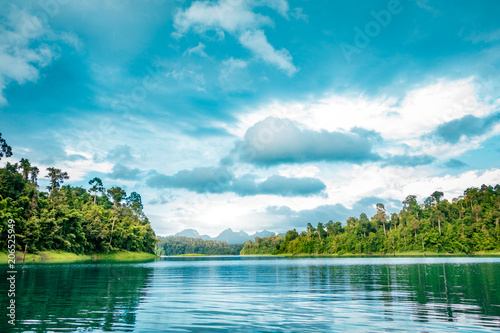 Mountain scenery with with tropical rain forest in the background and blue water lake in the foreground during a sunny day at Ratchaprapha Dam at Khao Sok National Park, Surat Thani Province, Thailand