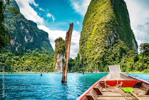 Wooden Thai traditional long-tail boat on a lake with mountains and rain forest in the background during a sunny day at Ratchaprapha Dam at Khao Sok National Park, Surat Thani Province, Thailand photo