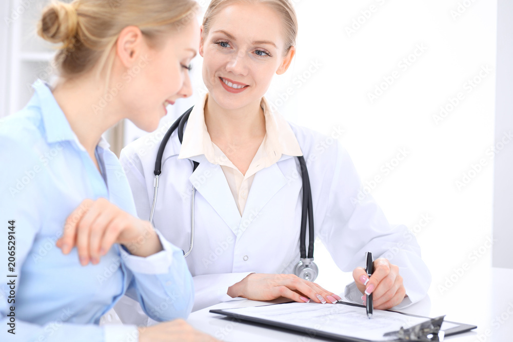 Blonde female doctor and patient talking in hospital office. Health care and client service in medicine Blonde female doctor and patient talking in hospital office. Health care and client service in medicine