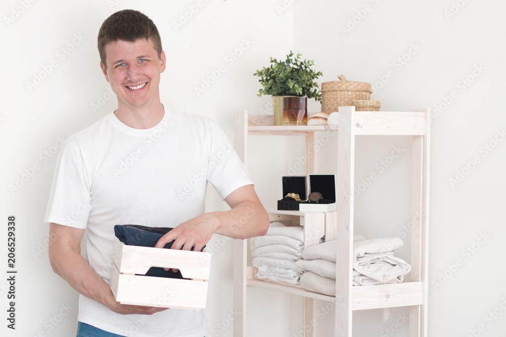 Young handsome European man with dark hair brings wardrobe order puts everything on its place hides things in boxes. Closet organized. Capsule wardrobe. Young handsome European man with dark hair brings wardrobe order puts everything on its place hides things in boxes. Closet organized. Capsule wardrobe.
