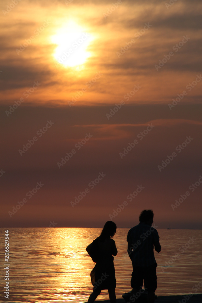Dark vertical picturesque shot of couple walking alone the beach, enjoying warm summertime evening, watching sunset, having good time together. Man and woman have promenade over beautiful embarkment.