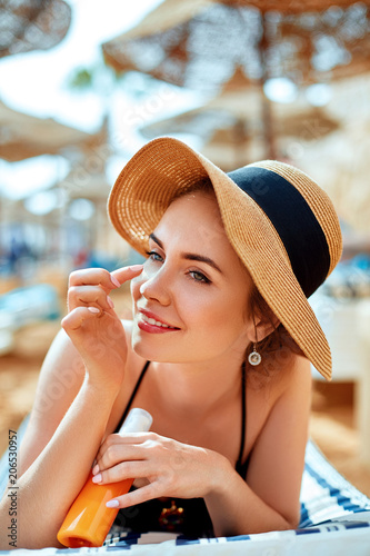 Suntan   woman in hat applying sunscreen solar. Beautiful happy woman smear  lotion  with sun cream   to her nose. Skincare.