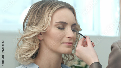 Professional make-up artist combing eyelashes of model in white room