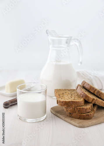 Bread on a cutting board with a glass jug of milk and a glass and cheese on a small plate. Selective focus. Blur