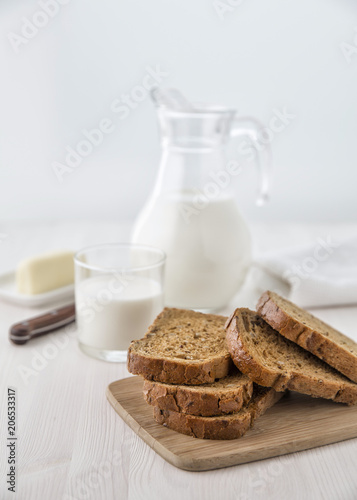 Bread on a cutting board with a glass jug of milk and a glass and cheese on a small plate. Selective focus. Blur