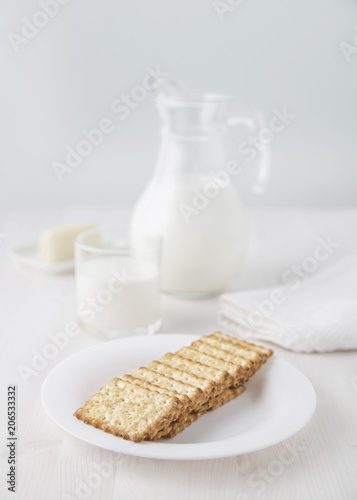 Crackers on a white plate with a glass jug of milk and a glass and cheese on a small plate Selective focus. Blur