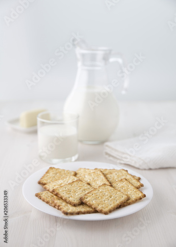Crackers on a white plate with a glass jug of milk and a glass and cheese on a small plate Selective focus. Blur