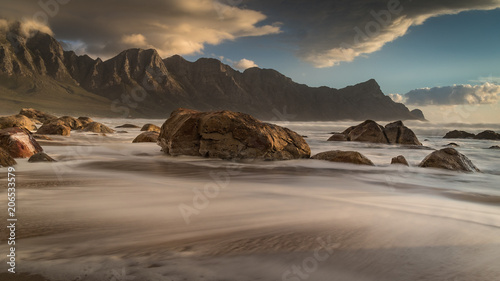 Rocky beach in the late afternoon sun with beautiful mountains in the background.