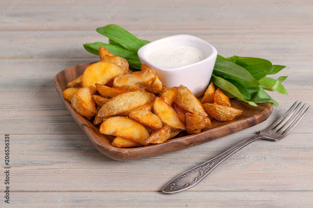 Slices of baked potatoes with leeks and garlic sauce in a wooden bowl
