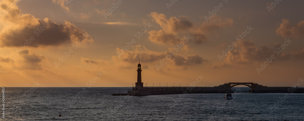 Silhouette shot of harbor entrance with lighthouse and bridge at sunrise time located in Montaza public Park, Alexandria, Egypt