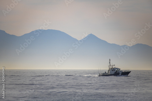 Beautiful sunrise over the ocean with boat and mountains in the background. © Global News Art