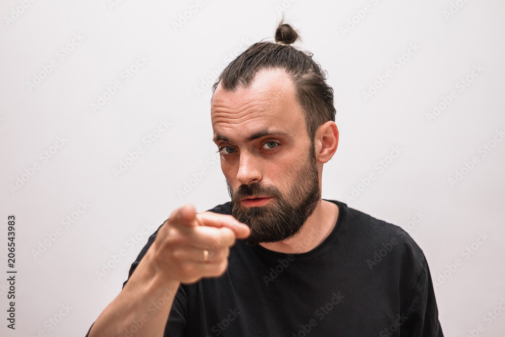 a man with a beard and a black t-shirt on a white background points forward with his index finger a man with a beard and a black t-shirt on a white background points forward with his index finger