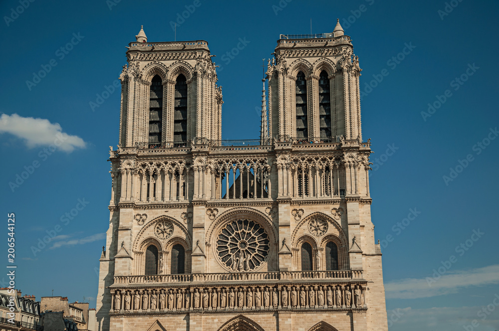 Towers and ornament on facade of gothic Notre-Dame Cathedral under sunny blue sky at Paris. Known as the “City of Light”, is one of the most impressive world’s cultural center. Northern France.