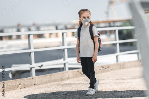child in protective mask walking on bridge, air pollution concept