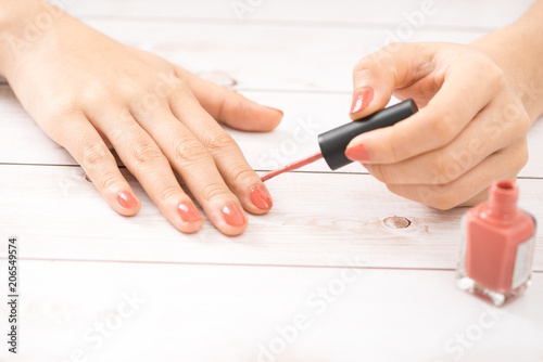 Female hands with red manicure and an open bottle of varnish on the table