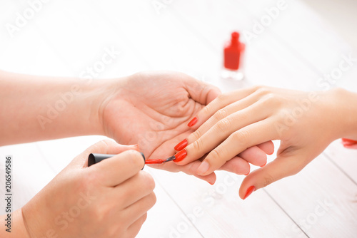 Woman getting nail manicure. Manicurist applying red nail polish to customer.