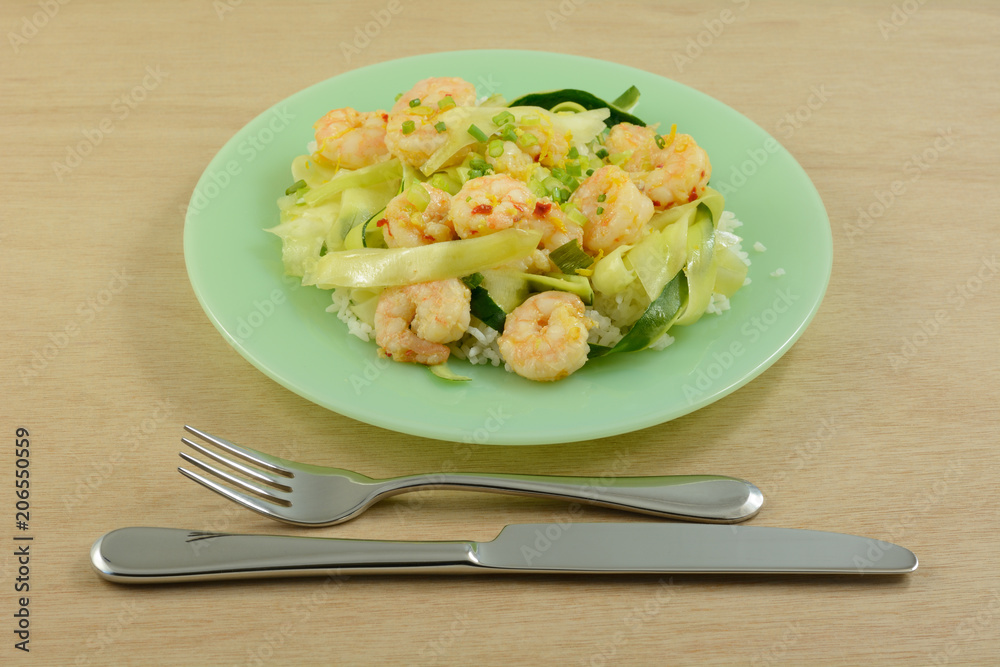 Shrimp and zucchini on rice on green plate with fork and knife on wooden table Shrimp and zucchini on rice on green plate with fork and knife on wooden table