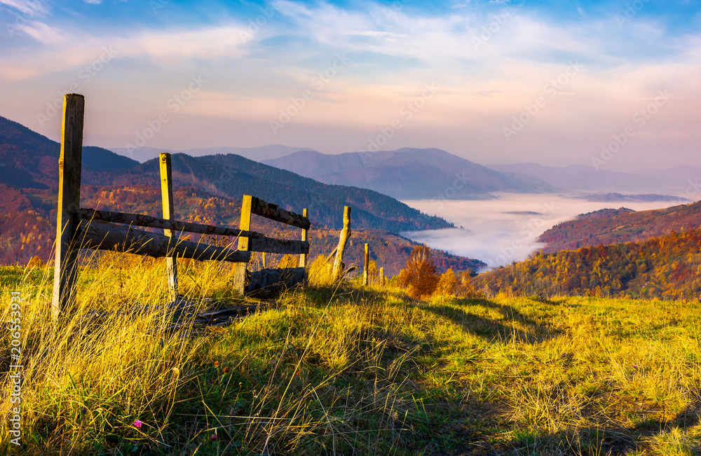 beautiful mountainous landscape with wooden fence. lovely autumnal scenery at sunrise with gorgeous sky over the valley full of fog