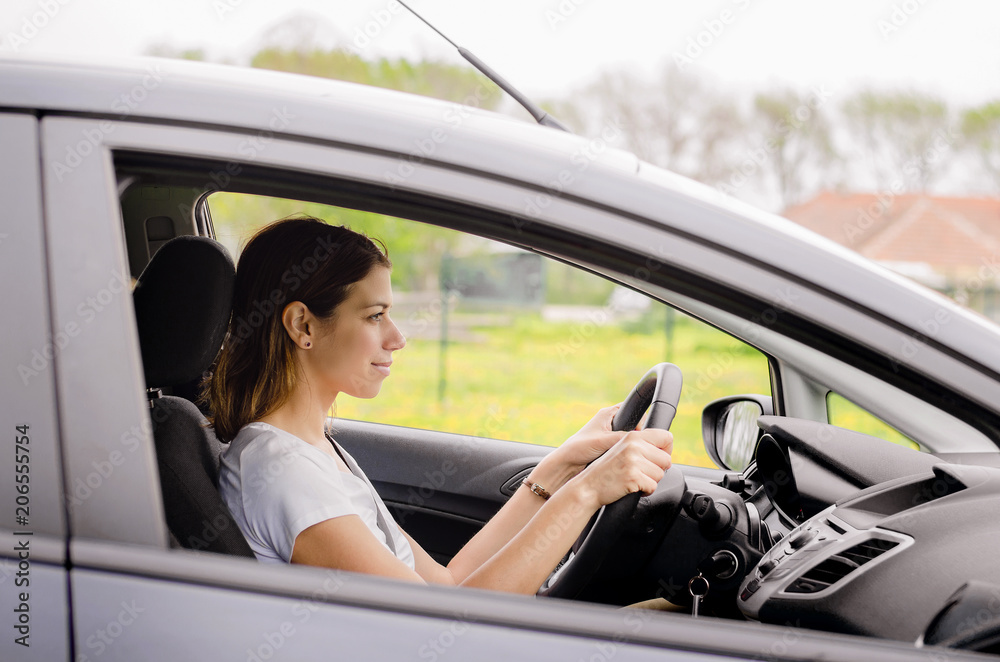 Young woman driving car, smiling.