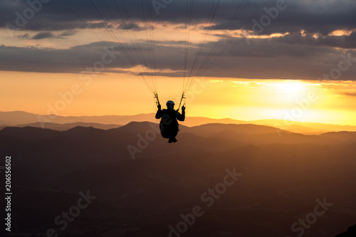 A paraglider silhouette flying against the sunset over Mt.Cucco 
