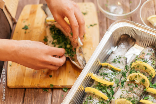 Woman’s hands preparing fish with greenery.