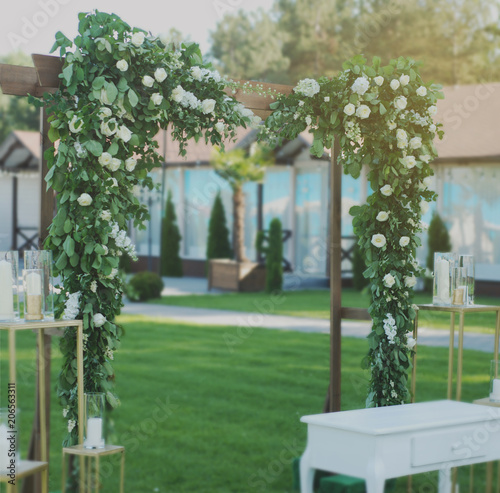 Rustic Wedding Ceremony Arch on the Open Area with Greem Grass. Wooden Arch with Flowers Arrangement
