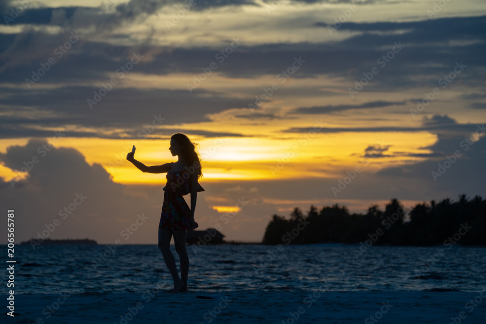 Girl on the beach, against a sunset background, makes a selfie