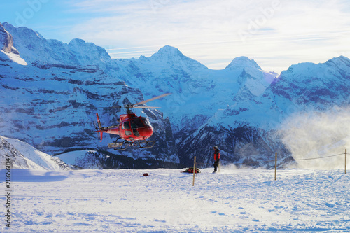 Red helicopter flying Swiss Alpine mountains Maennlichen in winter photo