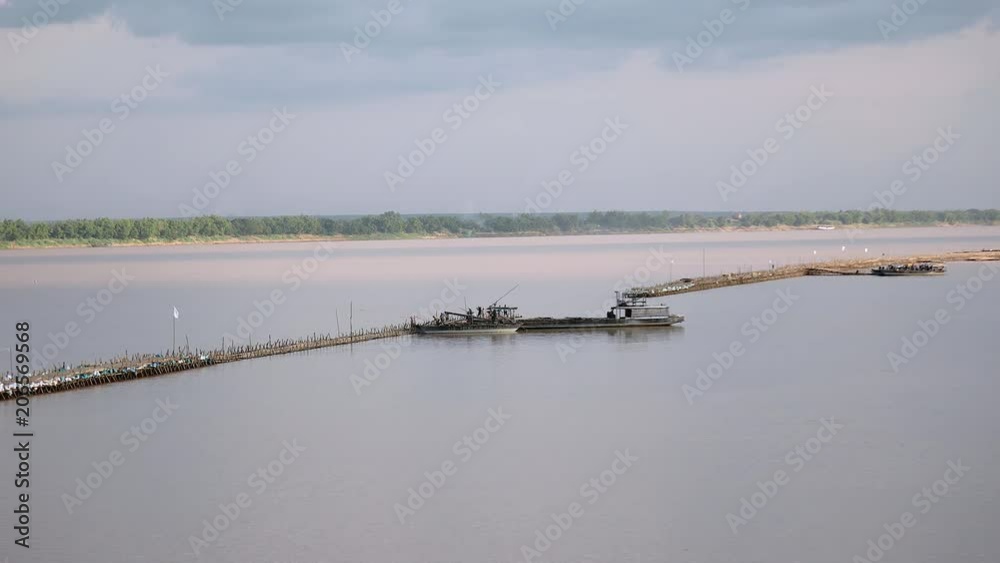 View riverside of the construction of the bamboo bridge. Workers are moving bamboo poles loaded in an old boat to a bridge.