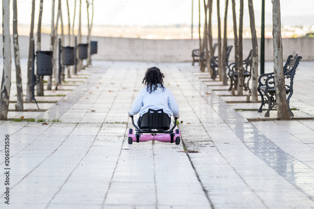 Obraz premium Hoverboard o patín eléctrico con sillín manejado por una niña morena rizosa mientras juega en el barrio