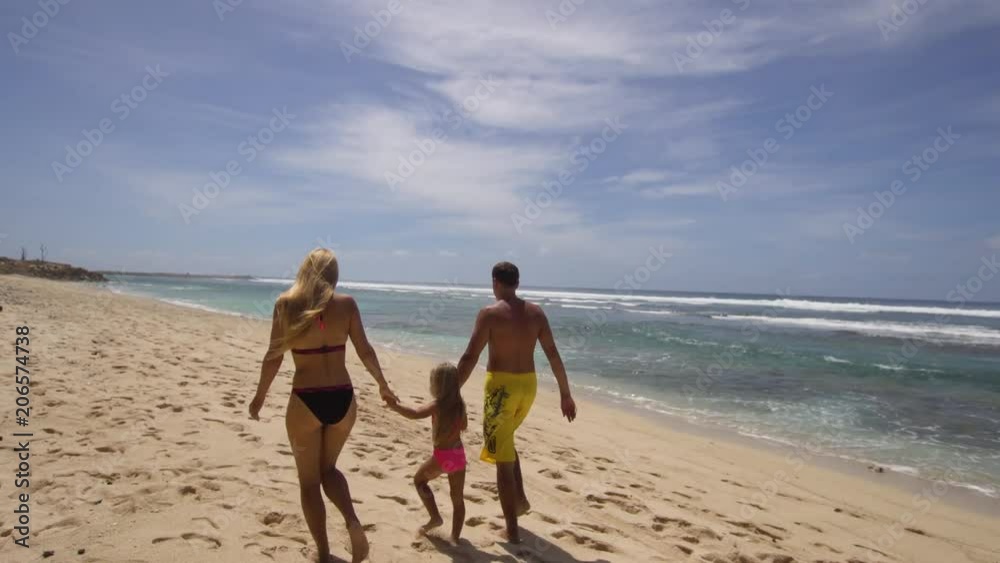 Happy beautiful family with child walking together on tropical beach during summer vacation. Bali. Family of three having fun on tropical beach. Travel concept. Family relationships Happy beautiful family with child walking together on tropical beach during summer vacation. Bali. Family of three having fun on tropical beach. Travel concept. Family relationships
