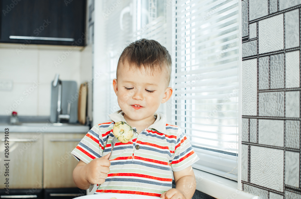 the child in the kitchen with a fork eating young potatoes the child in the kitchen with a fork eating young potatoes