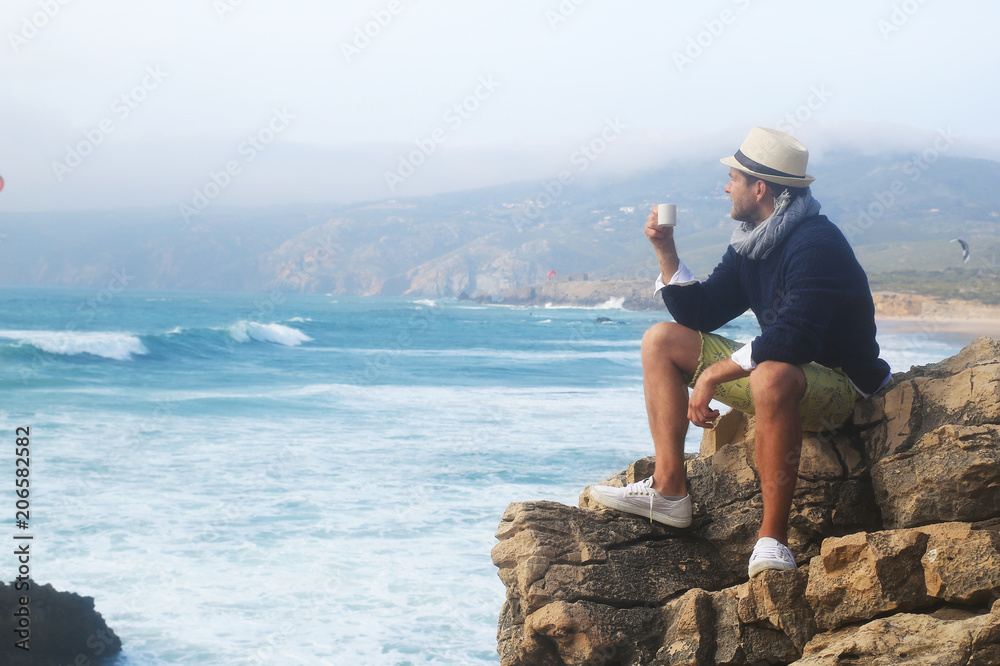 Man drinking coffee against the waves of the ocean