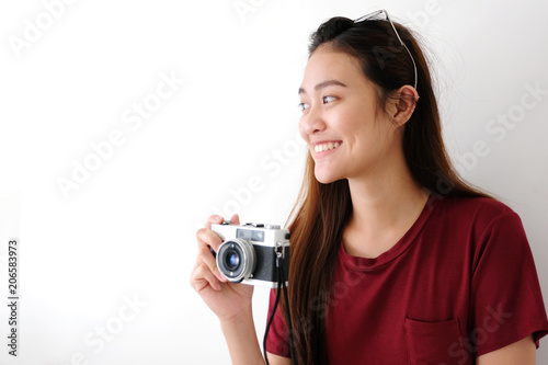 Young asian woman holding vintage camera with smiling face standing over white wall background with copy space, people positive expression, travel summer holiday vacation concept