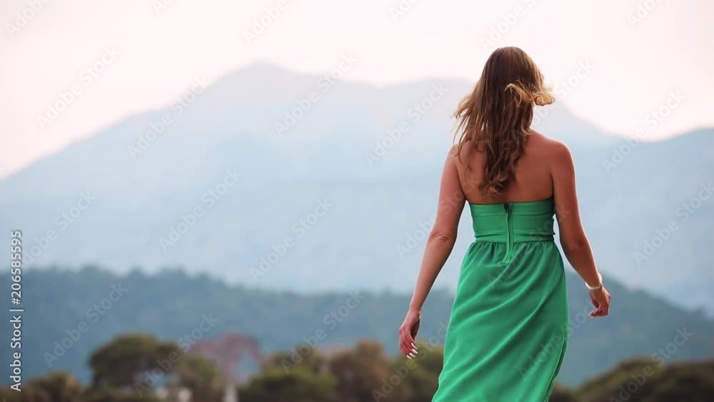 Beautiful woman in green dress looking at sea and mountains landscape Beautiful woman in green dress looking at sea and mountains landscape