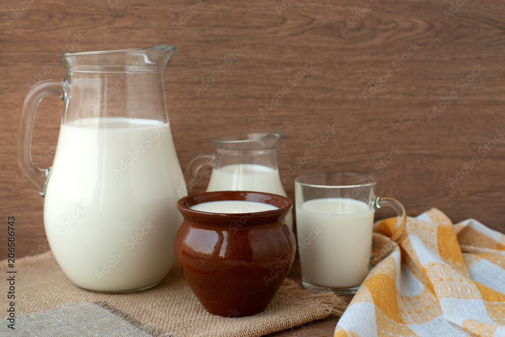 Milk in different dishes. Milk jugs, a glass and a clay pot in a rustic style. A lot of milk on sacking. Milk in different dishes. Milk jugs, a glass and a clay pot in a rustic style. A lot of milk on sacking.