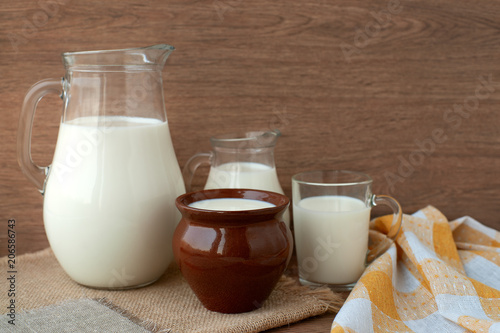 Milk in different dishes. Milk jugs, a glass and a clay pot in a rustic style. A lot of milk on sacking.