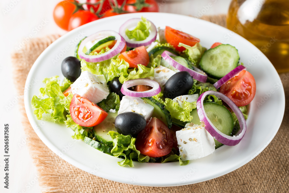 Fresh Greek salad made of cherry tomato, ruccola, arugula, feta, olives, cucumbers, onion and spices. Caesar salad in a white bowl on wooden background. Healthy organic diet food concept.