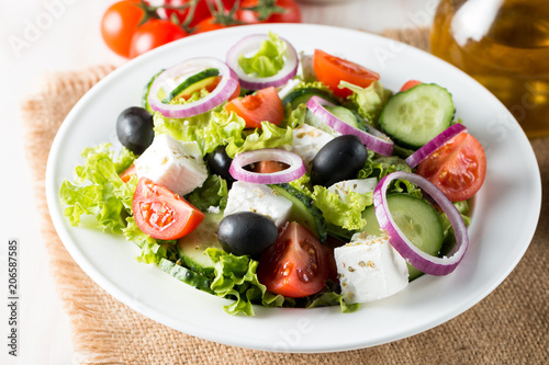 Fresh Greek salad made of cherry tomato, ruccola, arugula, feta, olives, cucumbers, onion and spices. Caesar salad in a white bowl on wooden background. Healthy organic diet food concept. © jeny_lk