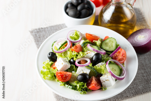 Fresh Greek salad made of cherry tomato, ruccola, arugula, feta, olives, cucumbers, onion and spices. Caesar salad in a white bowl on wooden background. Healthy organic diet food concept.