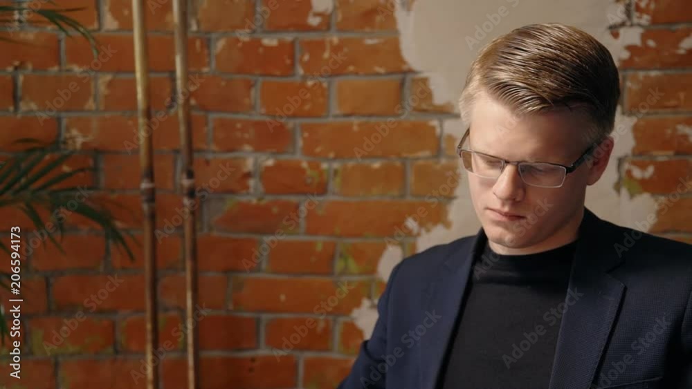 Portrait of young businessman in glasses reading paper contract in his office. Concept of: business people, reading glasses, office interior modern, document control