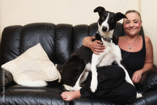 Happy woman petting her black & white dog on the couch at home in the living room