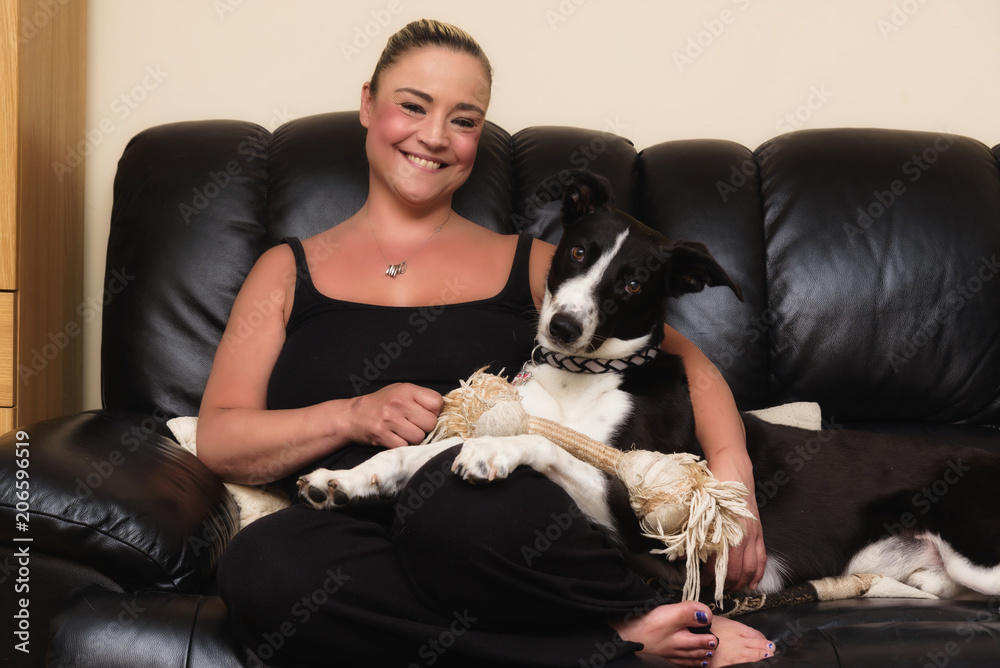 Happy woman cuddling her black & white dog on the couch at home in the living room Happy woman cuddling her black & white dog on the couch at home in the living room