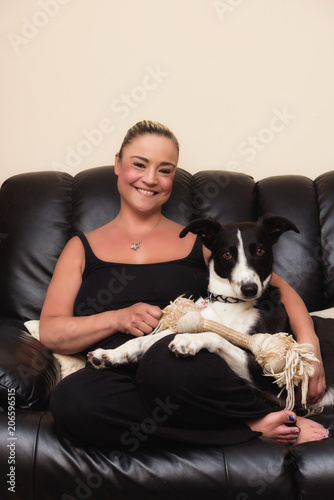 Happy woman cuddling her black & white dog on the couch at home in the living room